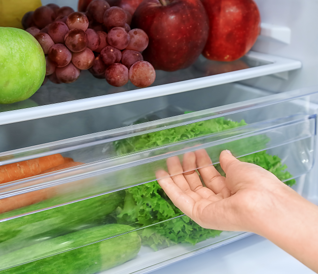 Photo of hand opening a refrigerator clear tray of vegetables